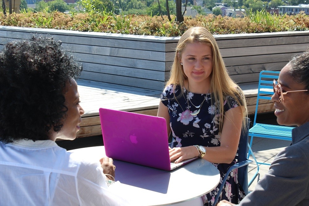 Camryn Hicks sits at a table with a pink laptop 
