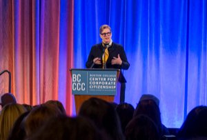 Katherine Smith speaking at a lectern in front of a colorfully lit curtain