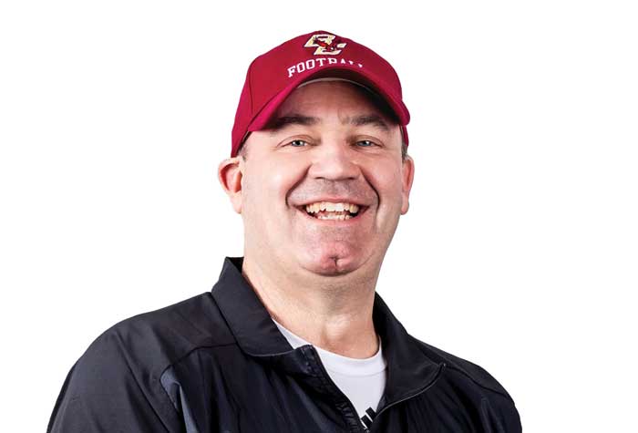 Coach Bill O'Brien laughing and holding a football.