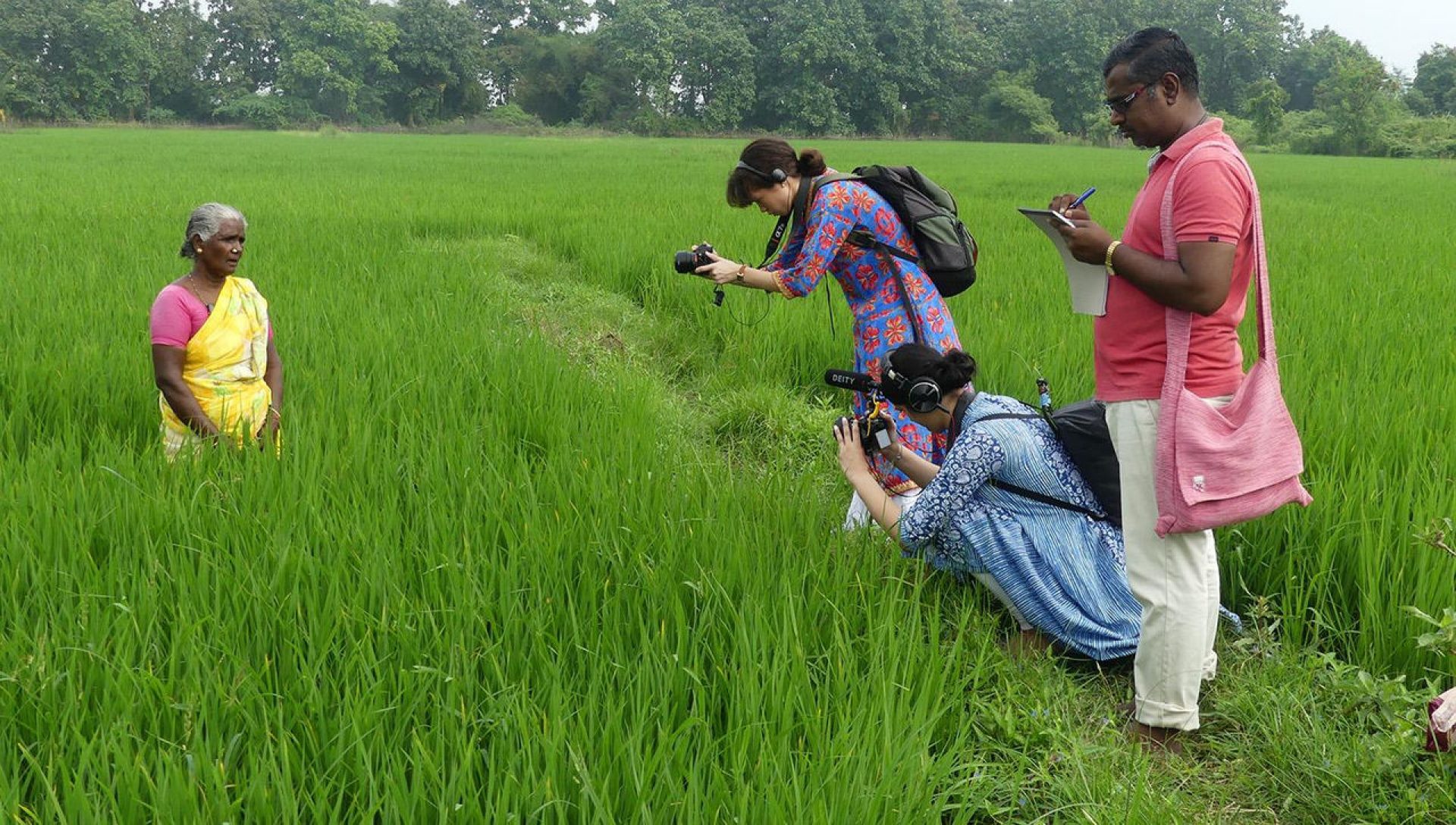 Three people filming a women in a green field