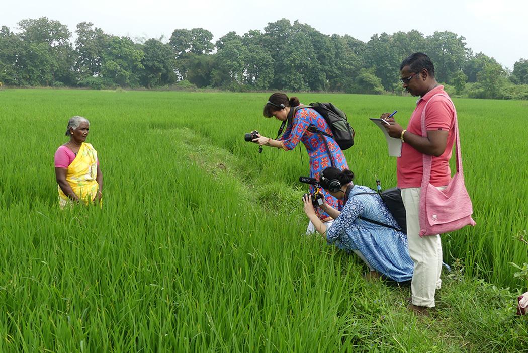 Three people filming a women in a green field